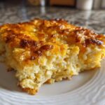 A close-up of a square serving of cheesy potato casserole with a golden brown, bubbly cheese topping.