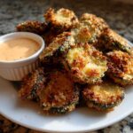 A plate piled high with crispy, golden brown Fried Pickles served next to a small ramekin of creamy dipping sauce.