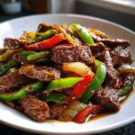 Close-up of tender beef strips coated in rich sauce with vibrant green and red peppers, showcasing the amazing pepper steak.
