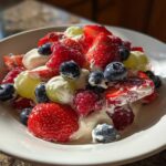 Close-up of a vibrant cheesecake fruit salad featuring strawberries, blueberries, raspberries, and grapes coated in a creamy dressing.