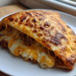 A close-up of a golden brown cheesy pocket taco, split open to show melted cheese and savory filling spilling out.