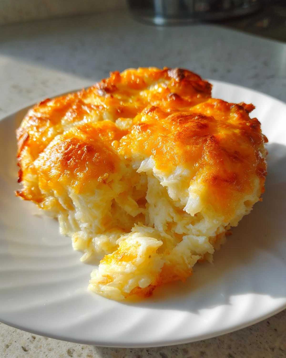 A scoop of creamy, shredded cheesy potato casserole with a bubbly, golden-brown cheese crust.