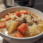 Close-up of a hearty bowl of turkey soup featuring shredded turkey, large chunks of potato, and bright orange carrots in broth.