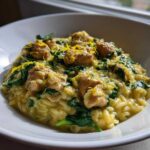 A close-up view of creamy lemon chicken orzo mixed with spinach and topped with bright lemon zest in a white bowl.