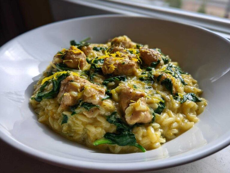 A close-up view of creamy lemon chicken orzo mixed with spinach and topped with bright lemon zest in a white bowl.
