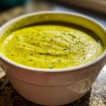 Close-up of a bowl of vibrant, creamy zucchini soup, garnished with pepper flakes.