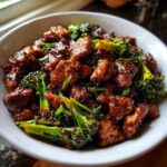 Close-up of glossy, saucy chicken and broccoli pieces served in a white bowl.