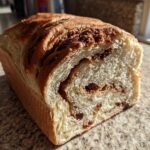 A loaf of homemade raisin bread, sliced to show the swirl of cinnamon filling and plump raisins inside.
