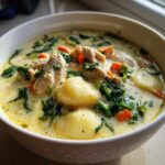 Close-up of a bowl of creamy olive garden chicken gnocchi soup, showing chicken pieces, spinach, carrots, and dumplings.