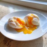 Two perfectly poached eggs cut open on a white plate, showing bright, runny yolks spilling out.