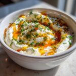A close-up of creamy ricotta dip drizzled with spicy honey and topped with fresh chives.