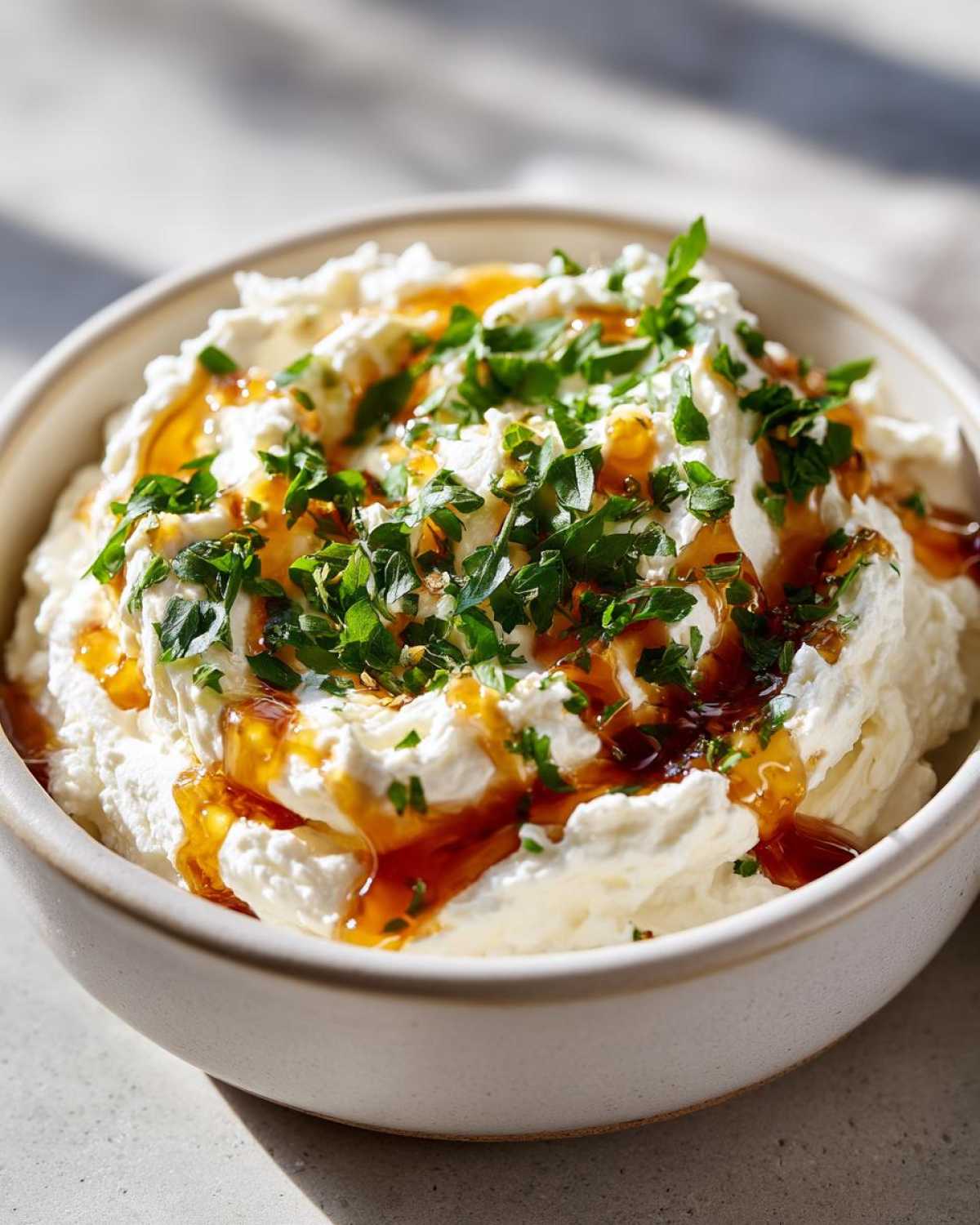 Close-up of a creamy ricotta dip drizzled with amber honey and topped with fresh chopped parsley.