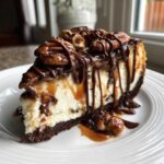 A rich slice of turtle cheesecake with a dark crust, creamy filling, topped with pecans, caramel, and chocolate drizzle.