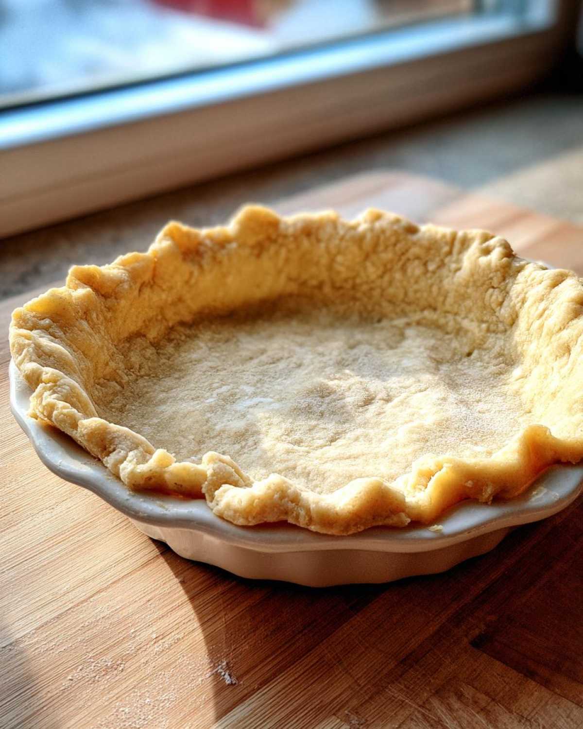 Close-up of an unbaked, fluted butter pie crust resting in a white ceramic pie dish.