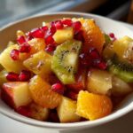 Close-up of a vibrant winter fruit salad featuring kiwi, orange segments, apple chunks, and bright pomegranate seeds.