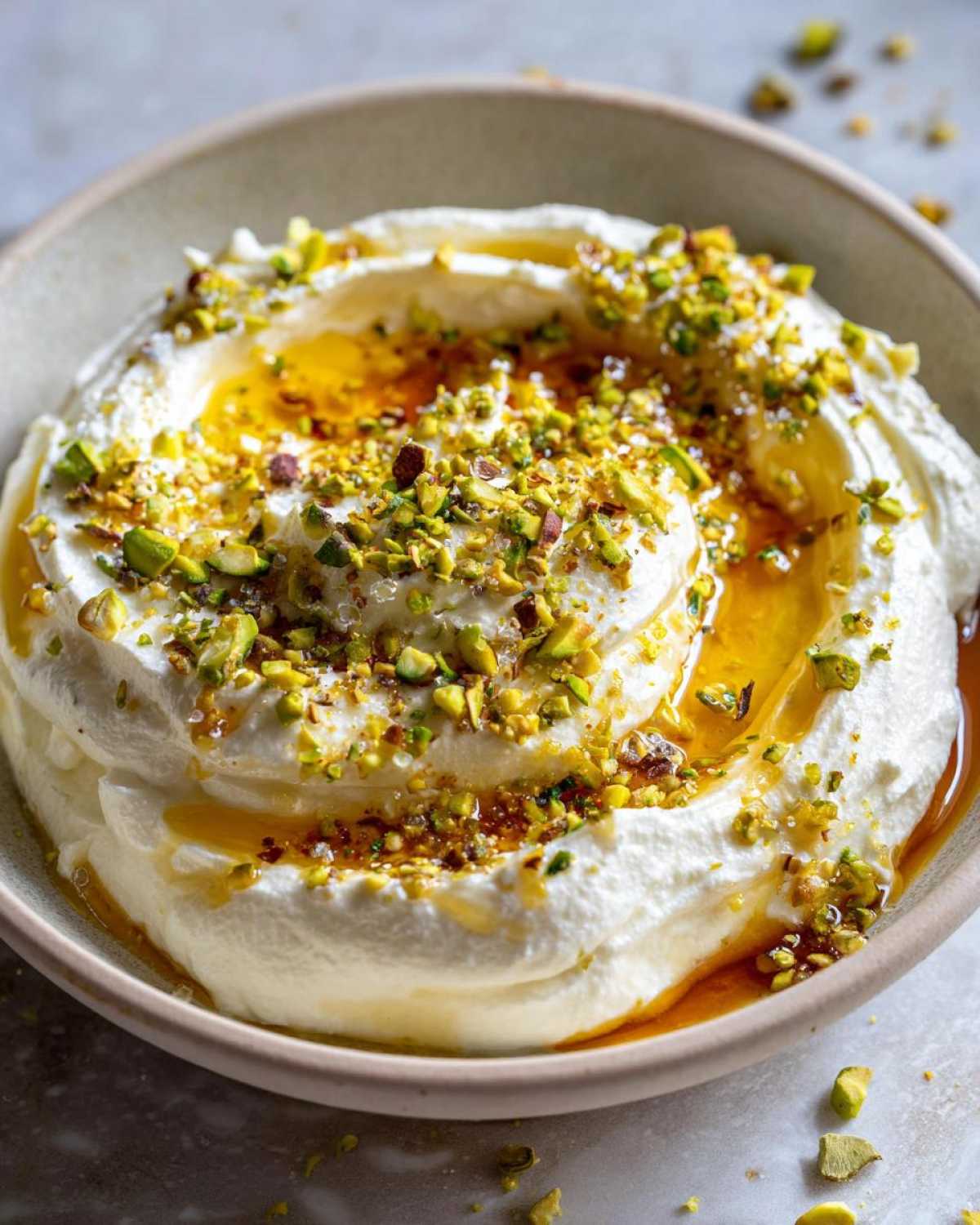 Close-up of creamy whipped feta dip swirled in a bowl, drizzled with honey and topped with chopped pistachios.