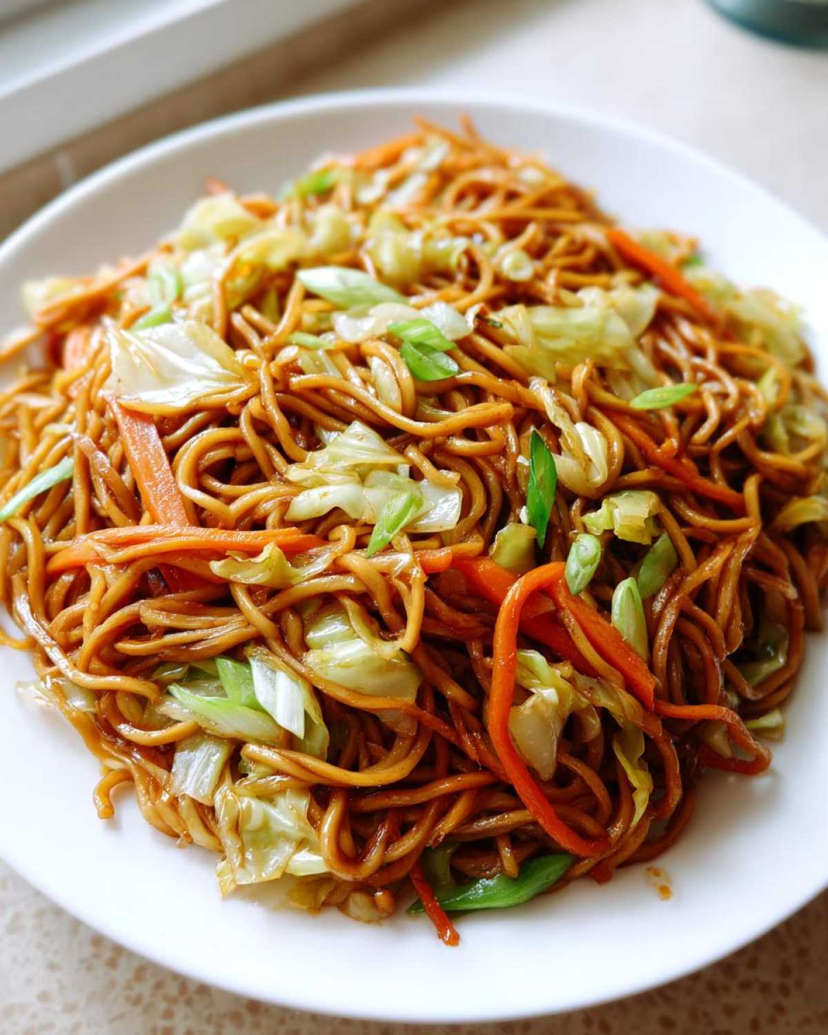 A close-up view of a plate piled high with delicious, savory fried noodles mixed with shredded cabbage and carrots.