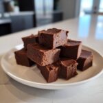 A stack of rich, dark chocolate fudge squares piled high on a white plate.
