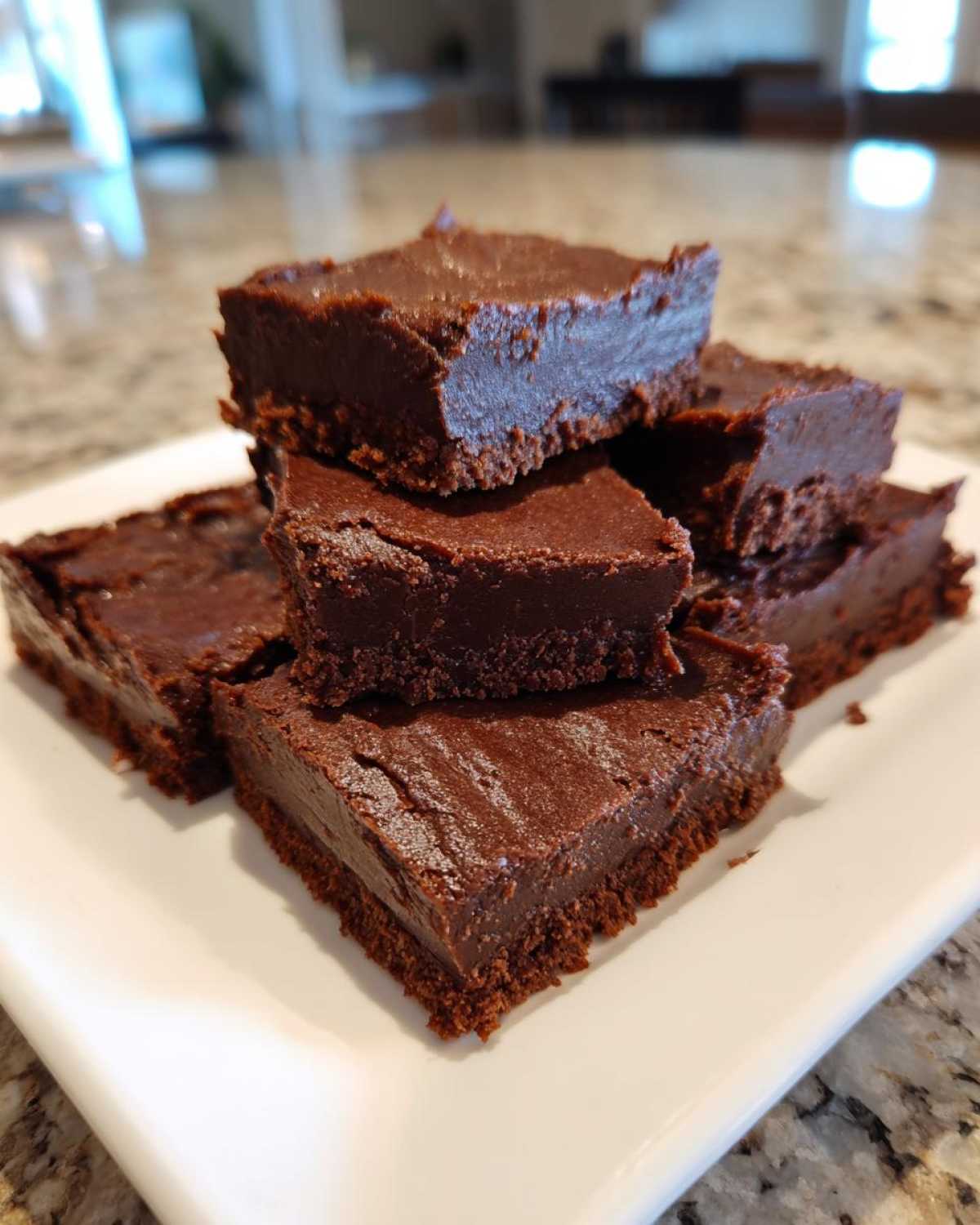 A stack of rich, dark chocolate squares of 3-ingredient fudge piled on a white plate.