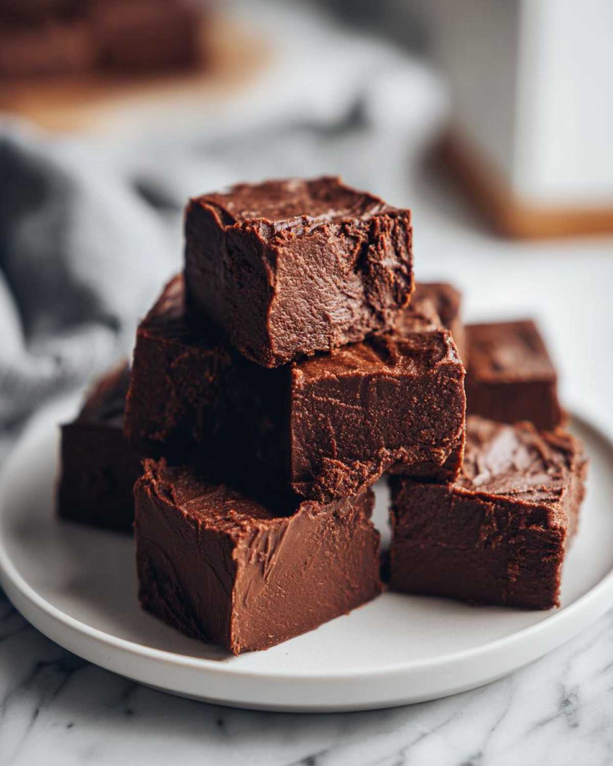 A stack of rich, dark chocolate fudge squares piled high on a white plate.