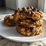 A stack of three chewy, oat-based breakfast cookie treats topped with chocolate chips on a white plate.
