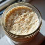 Overhead view of a thriving, bubbly sourdough starter in a glass jar, indicating peak activity.