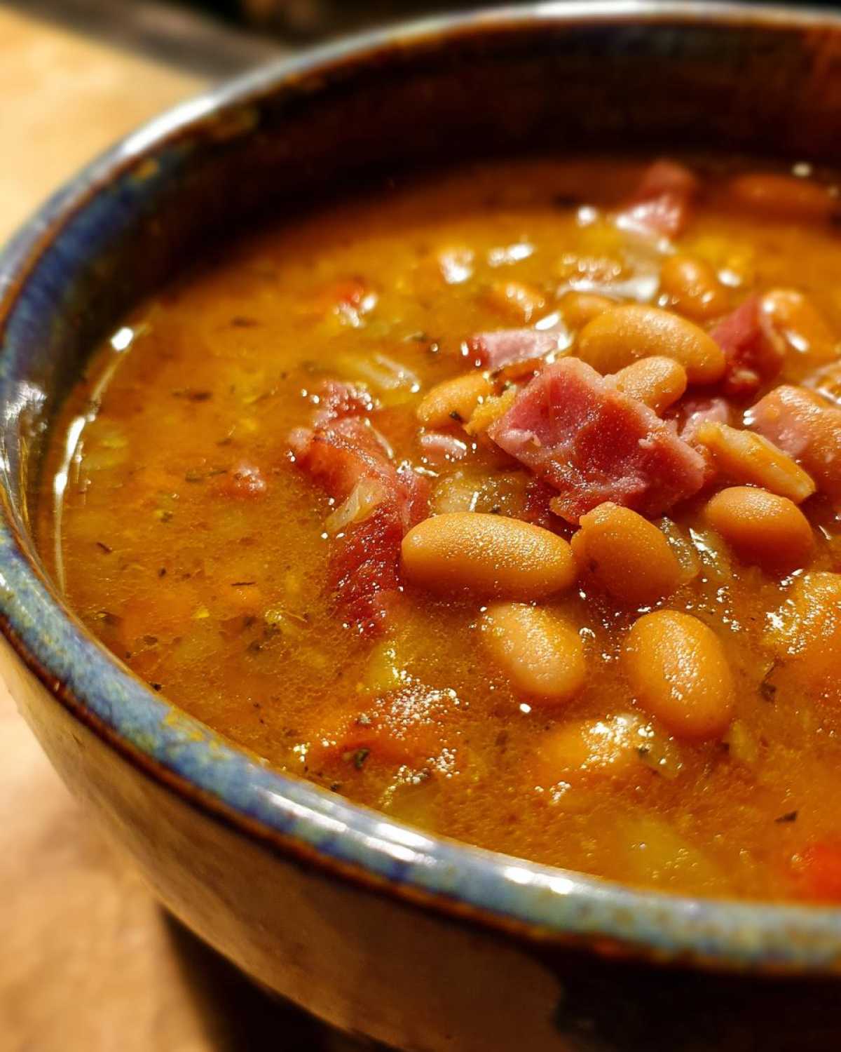 Close-up of a rustic bowl filled with thick, savory amazing 15 bean soup topped with chunks of ham.