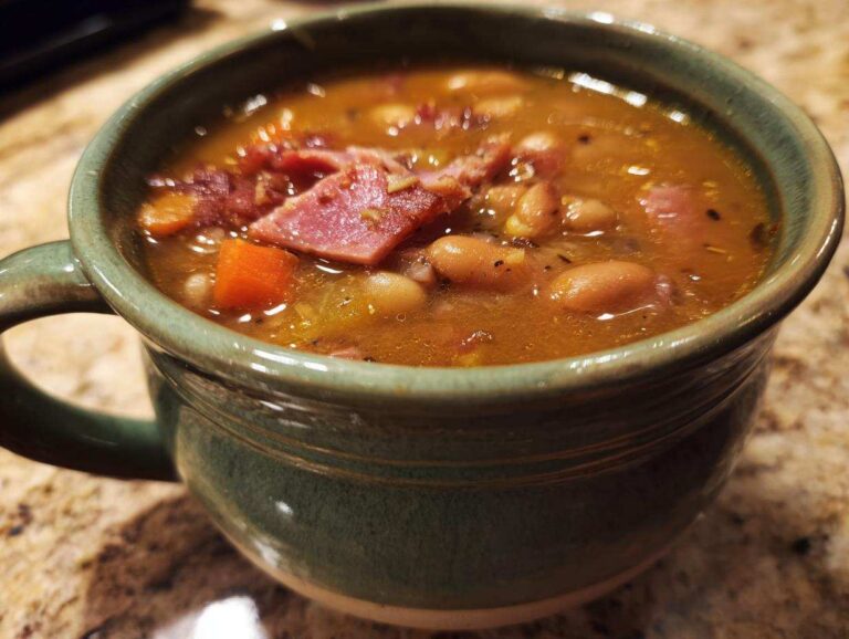 Close-up of a steaming bowl of amazing 15 bean soup, featuring beans, carrots, and chunks of ham.