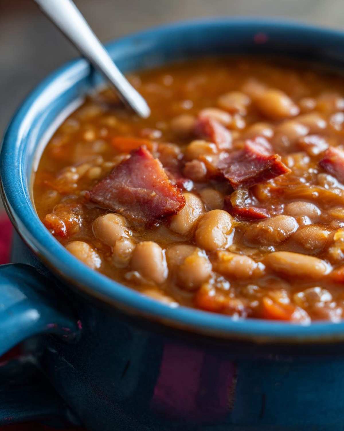 Close-up of a rich, thick serving of 15 bean soup, featuring white beans and chunks of ham in a blue mug.
