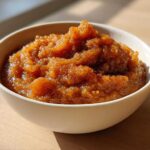 A close-up of thick, rich brown homemade applesauce piled high in a white bowl.