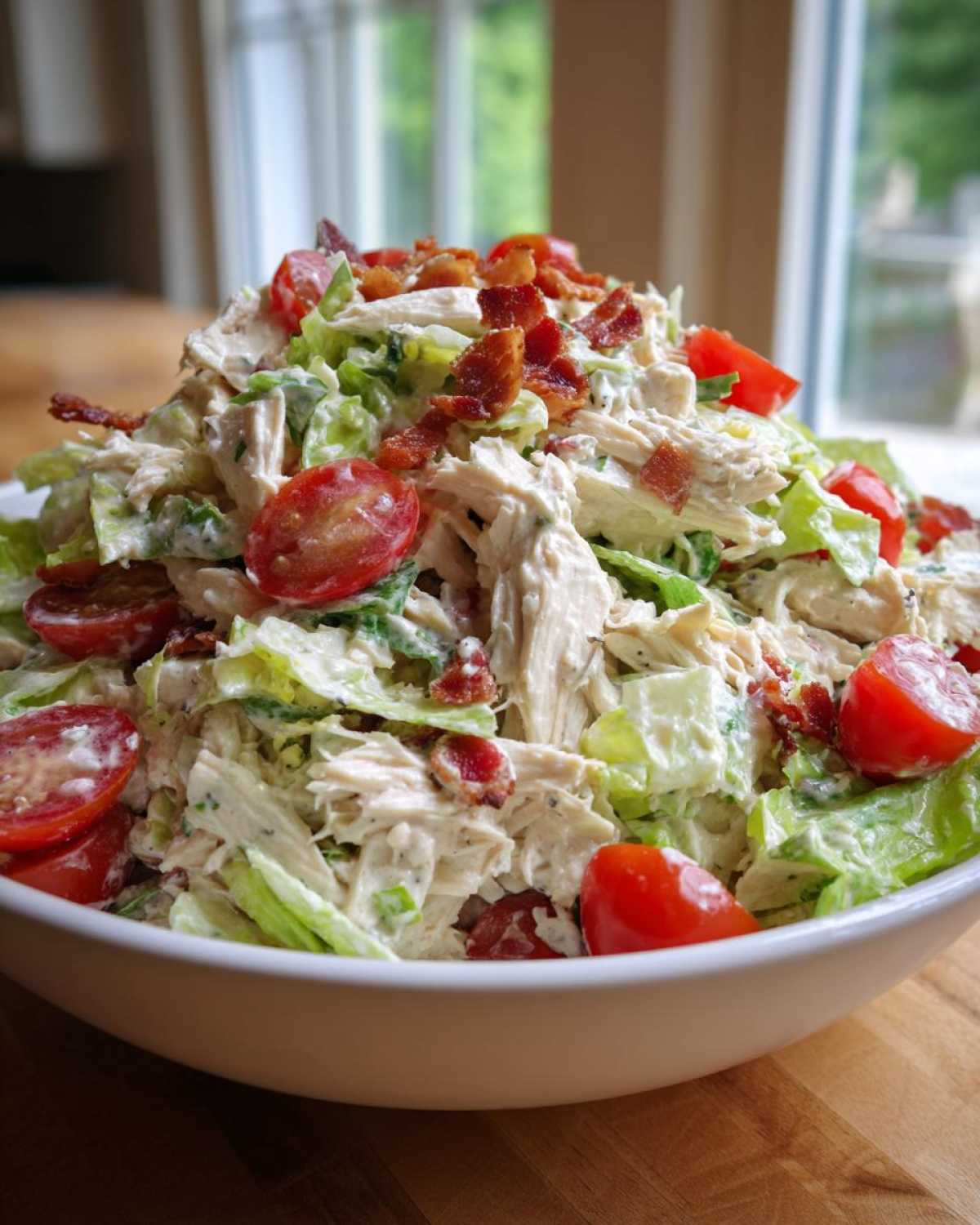 A generous serving of amazing blt chicken salad featuring shredded chicken, crisp lettuce, halved cherry tomatoes, and bacon bits in a white bowl.