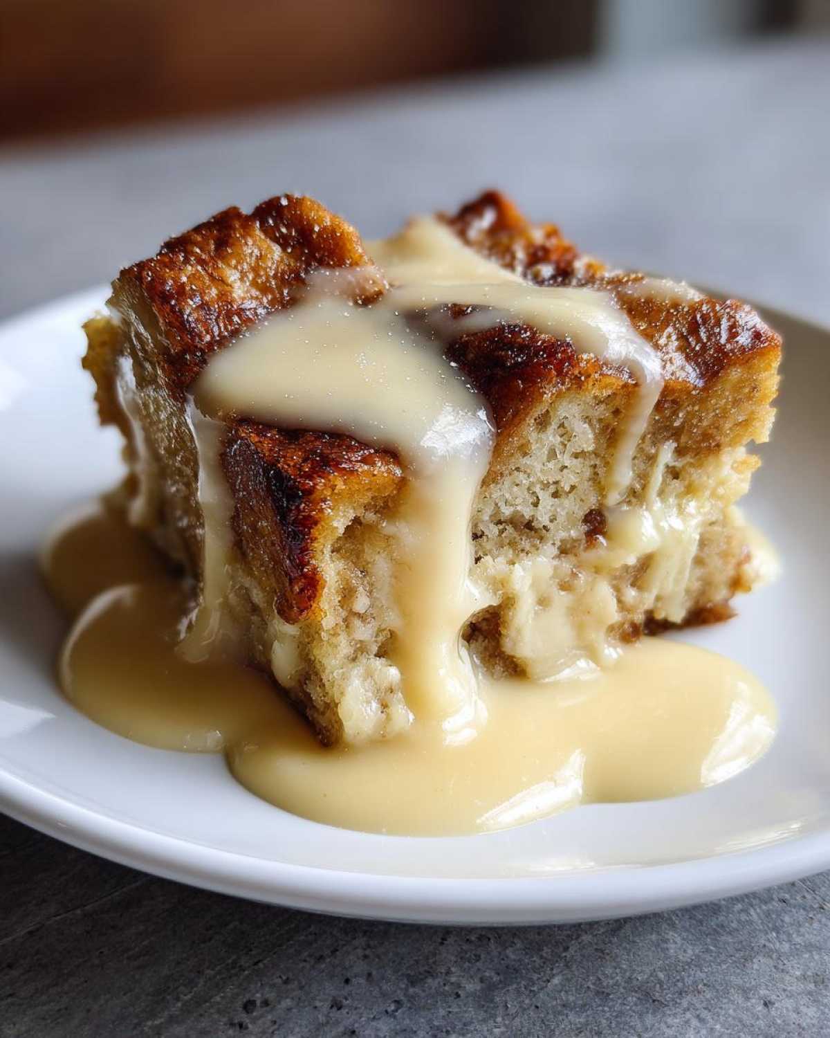 A close-up of a square slice of amazing bread pudding topped with rich vanilla sauce.