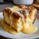 A close-up of a slice of amazing bread pudding generously covered in flowing vanilla custard sauce.