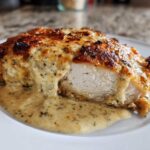 Close-up of a perfectly cooked caesar chicken breast, sliced to show the white meat and covered in a creamy, cheesy Caesar sauce.