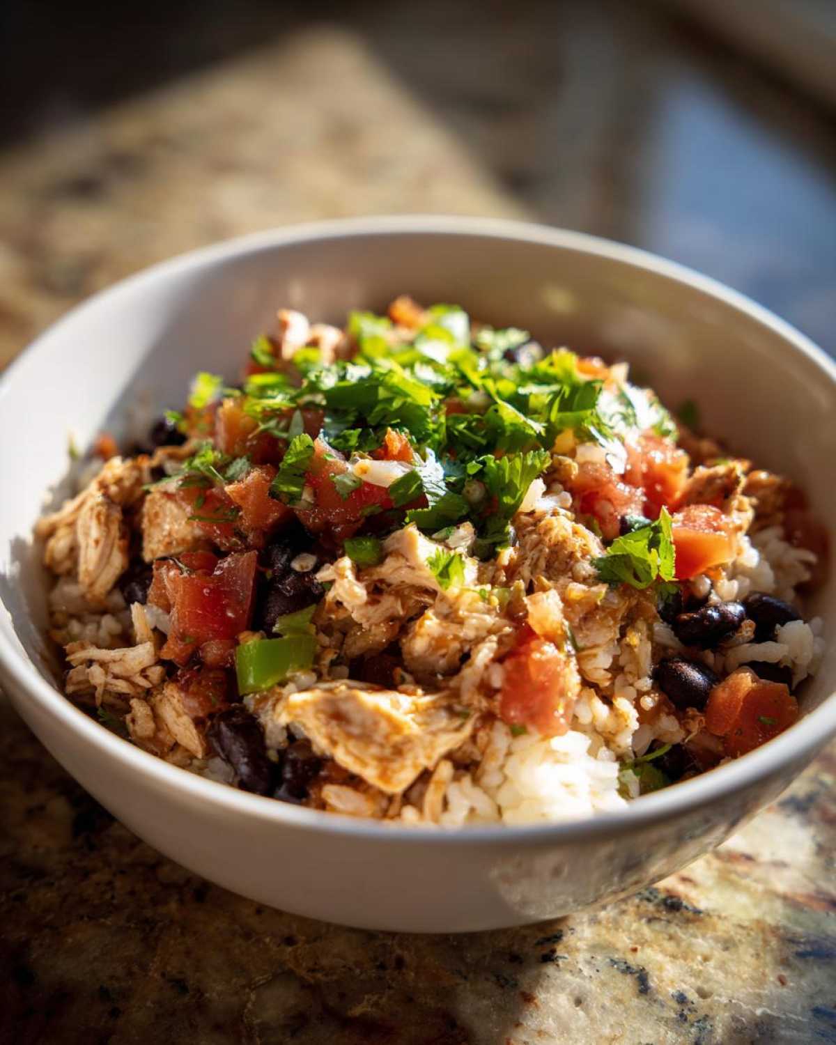 A close-up view of a white bowl filled with a delicious chicken burrito bowl, topped with pico de gallo and cilantro.