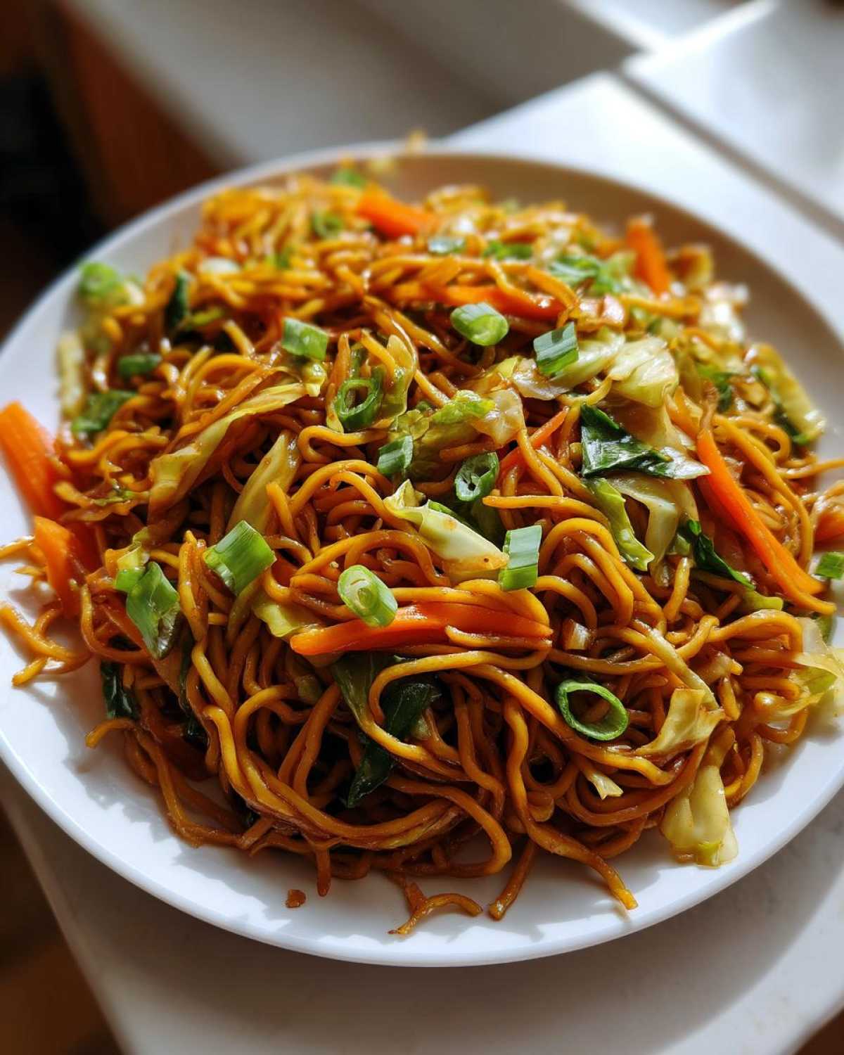 A close-up view of a generous serving of delicious fried noodles mixed with cabbage, carrots, and green onions.