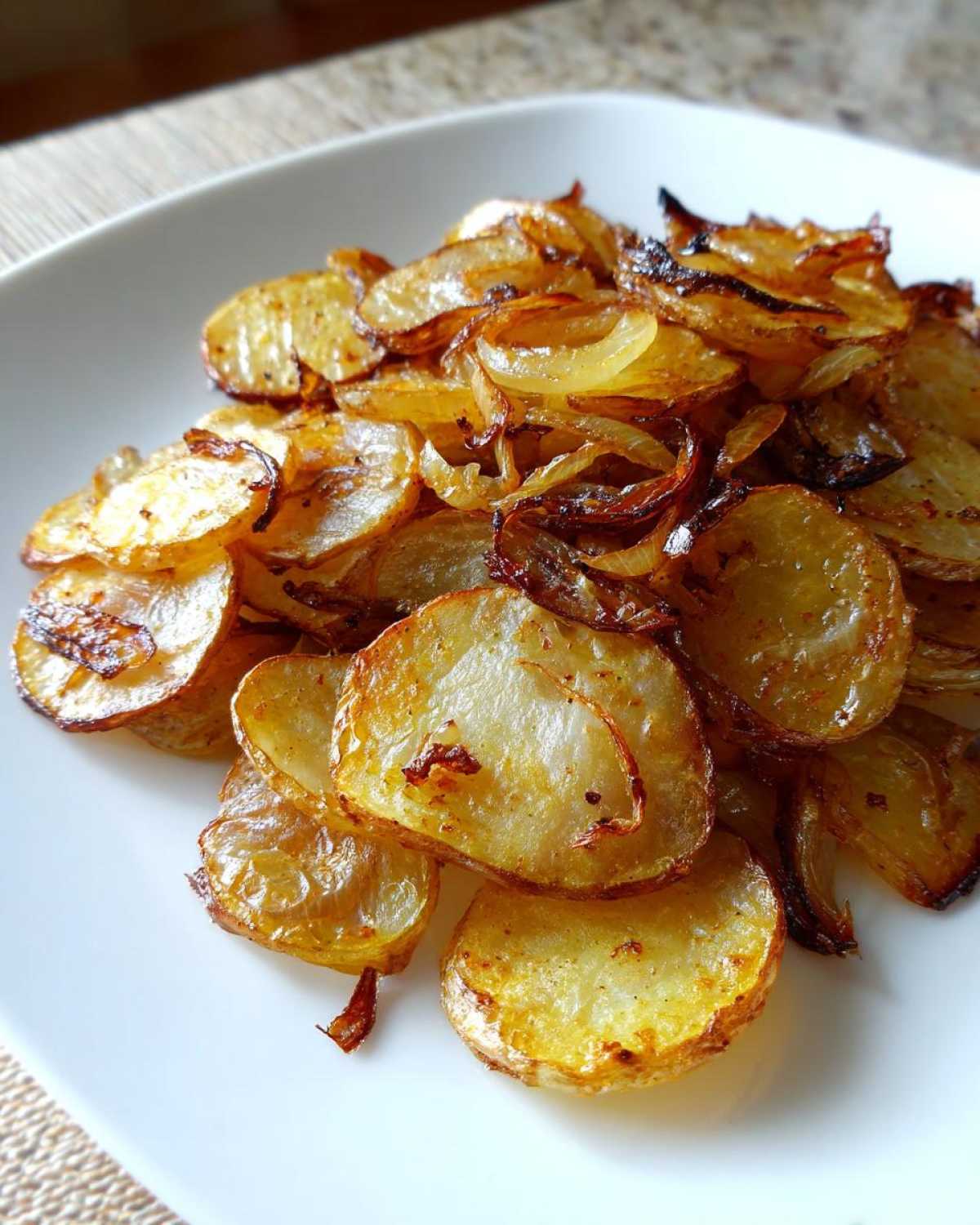 Close-up of golden brown, thinly sliced fried potatoes mixed with caramelized onions on a white plate.