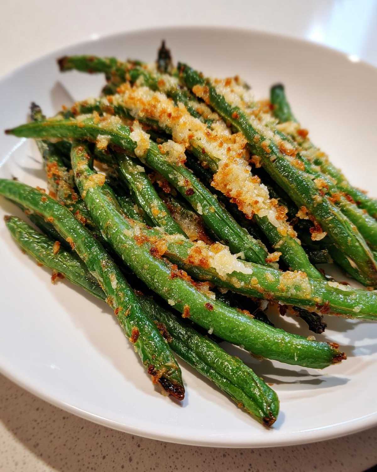 Close-up of bright green beans topped with crispy, golden breadcrumbs served on a white plate.