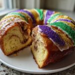 A delicious homemade king cake with a slice removed, showing the cinnamon swirl interior and purple, green, and gold sprinkles.