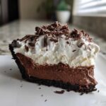 A decadent slice of mud pie featuring a dark chocolate crust, rich chocolate filling, and a thick layer of whipped cream topped with chocolate shavings.