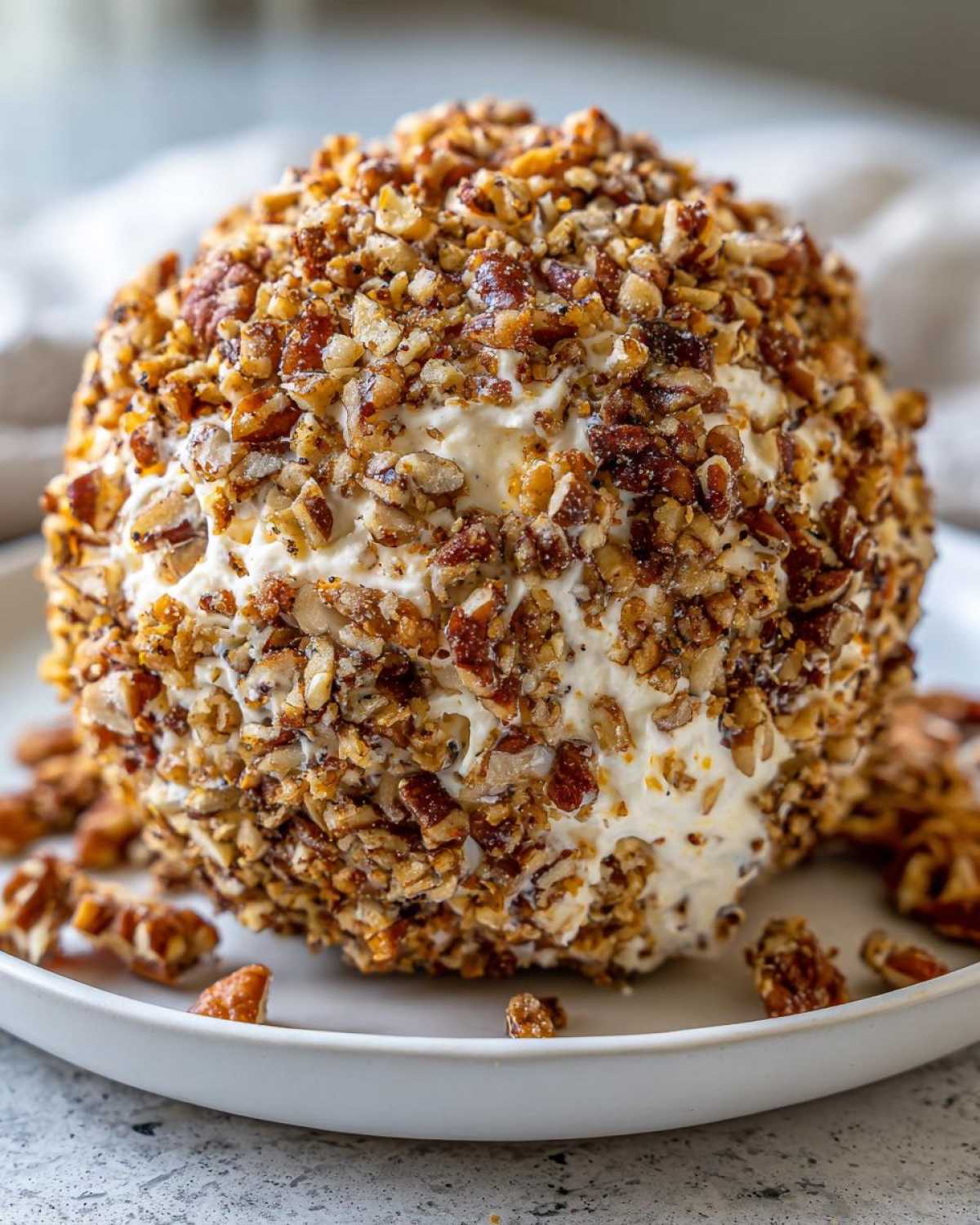 A close-up of a large, round cheese ball recipe coated entirely in chopped, toasted pecans.