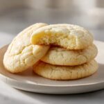 A stack of four amazing soft sugar cookies, with the top cookie having a bite taken out to show the soft, chewy interior.