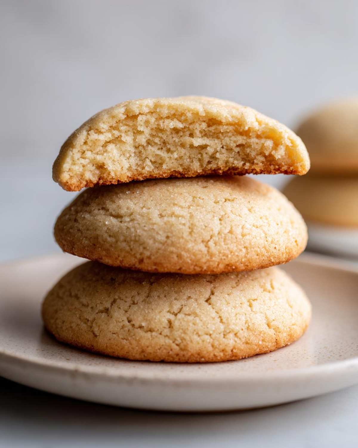 Close-up of three stacked soft sugar cookies, with the top one broken in half showing the fluffy interior texture.