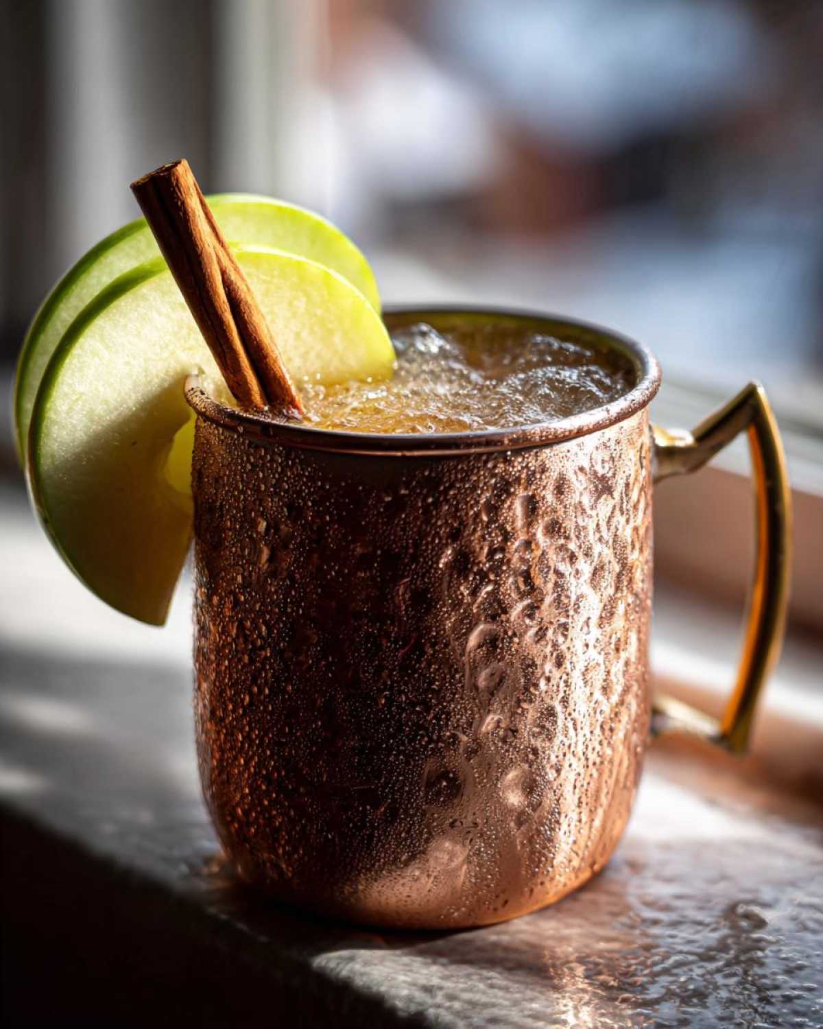 A frosty copper mug filled with an apple cider moscow mule, garnished with green apple slices and a cinnamon stick.