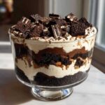 A decadent Baileys Chocolate Cheesecake Trifle layered with chocolate cake, cream, and topped with cookie crumbles.