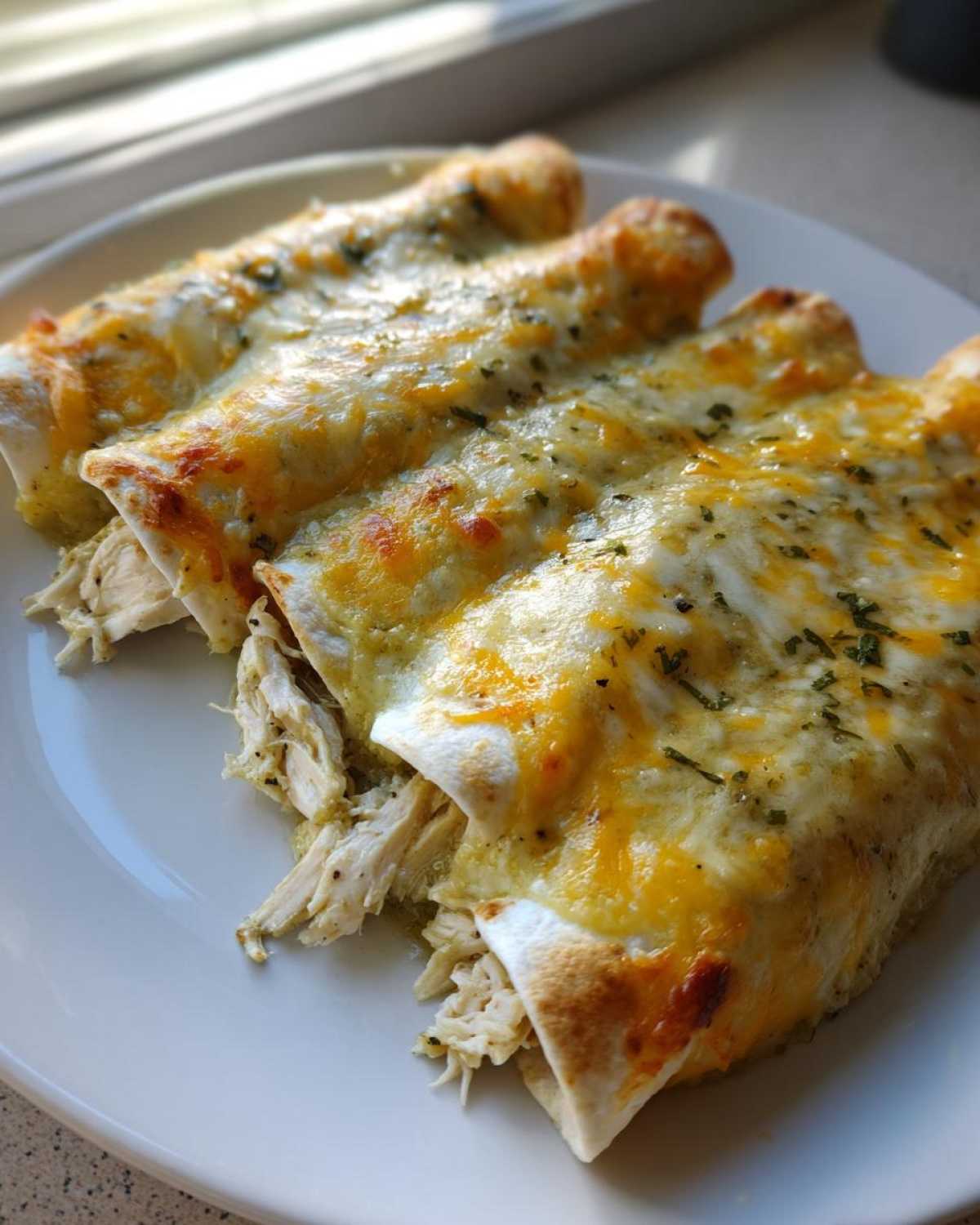 Close-up of three baked green chile chicken enchiladas covered in melted white and cheddar cheese.