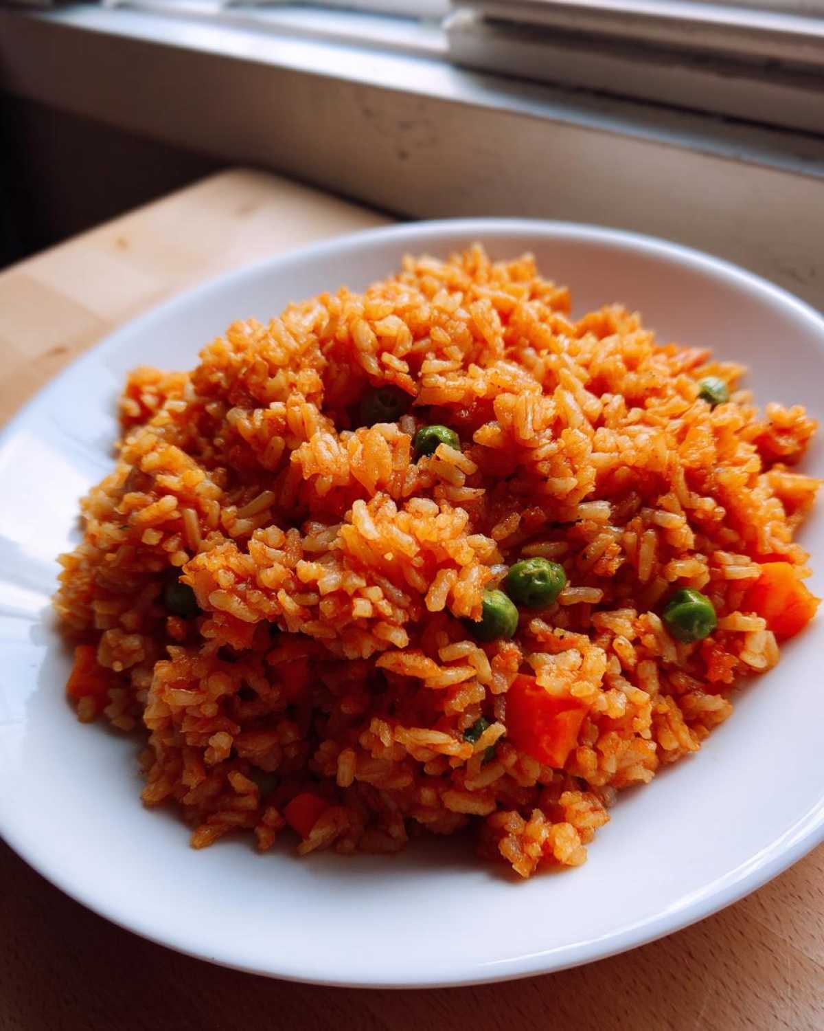 Close-up of a white bowl filled with vibrant orange Spanish rice mixed with green peas and diced carrots.