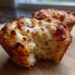 Close-up of a bitten Pizza Muffin showing a fluffy interior and browned, melted cheese topping.