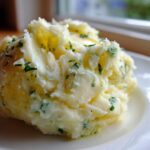 A close-up serving of creamy Boursin mashed potatoes mixed with green herbs on a white plate.