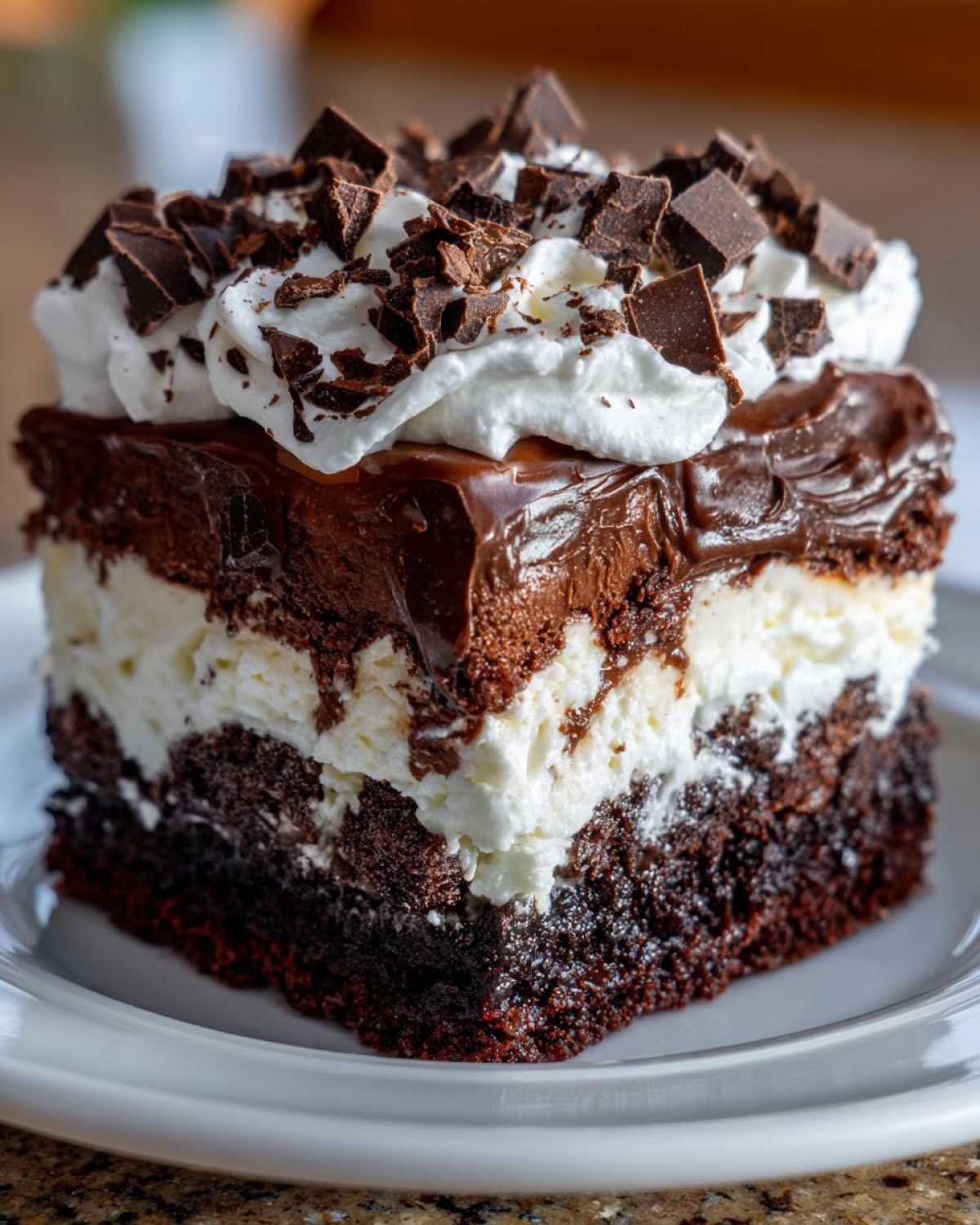 Close-up of a rich, layered brownie refrigerator cake slice topped with whipped cream and chocolate chunks.